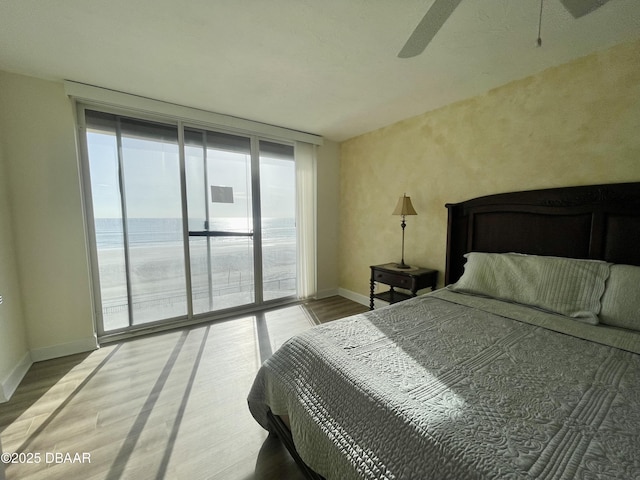 bedroom featuring access to exterior, hardwood / wood-style flooring, a water view, ceiling fan, and expansive windows