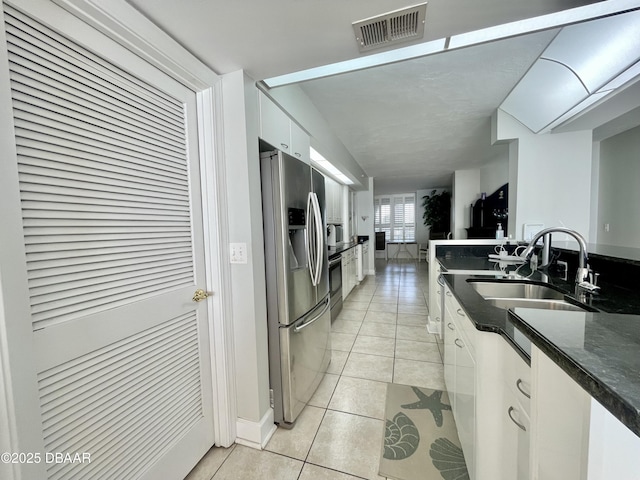 kitchen featuring stainless steel refrigerator with ice dispenser, sink, white cabinetry, dark stone counters, and light tile patterned floors