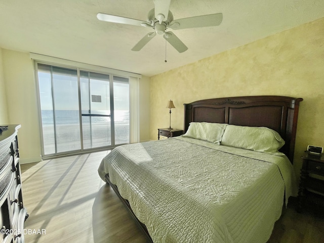 bedroom with hardwood / wood-style floors, a water view, access to outside, floor to ceiling windows, and ceiling fan