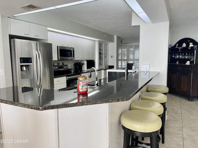 kitchen with light tile patterned floors, a breakfast bar, white cabinets, and stainless steel appliances