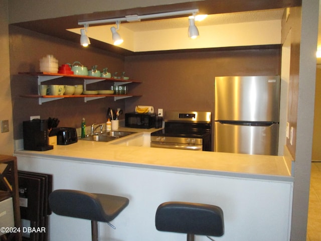 kitchen with sink, rail lighting, stainless steel appliances, kitchen peninsula, and a breakfast bar