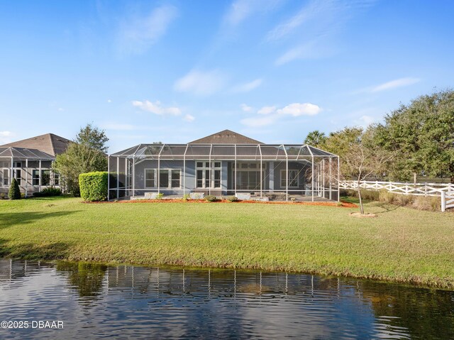 rear view of house featuring a water view, a lanai, and a lawn