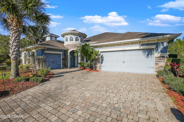 view of front of property featuring stone siding, decorative driveway, and an attached garage