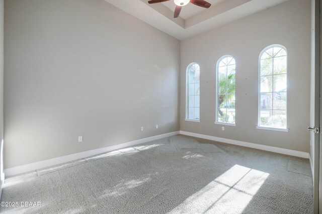 unfurnished room featuring baseboards, a raised ceiling, a ceiling fan, and light colored carpet