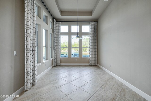 spare room with a towering ceiling, light tile patterned floors, baseboards, and a raised ceiling