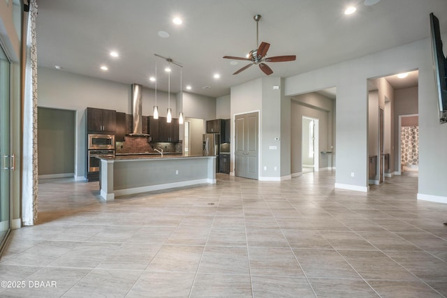 kitchen with dark brown cabinetry, open floor plan, appliances with stainless steel finishes, wall chimney exhaust hood, and a center island with sink