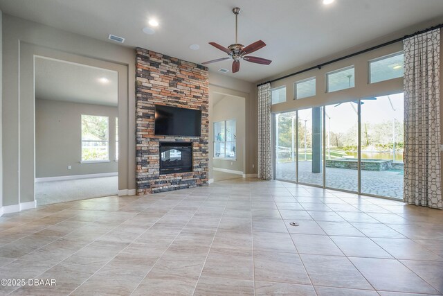 unfurnished living room featuring light tile patterned flooring, ceiling fan, a stone fireplace, and baseboards