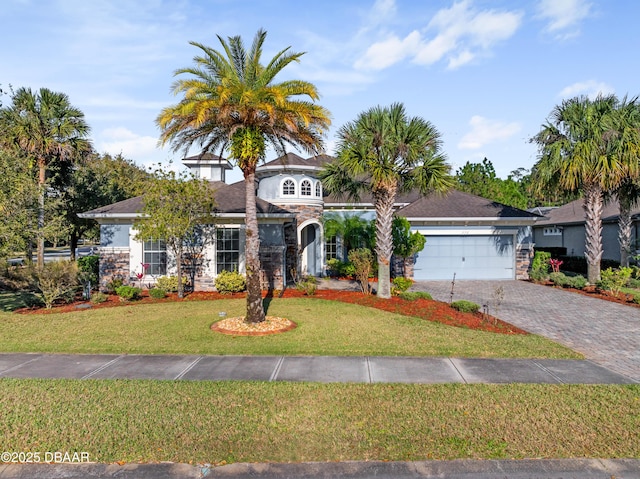 view of front of house with an attached garage, stone siding, decorative driveway, and a front yard