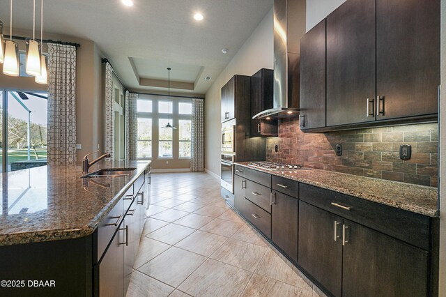 kitchen featuring pendant lighting, a raised ceiling, appliances with stainless steel finishes, a sink, and dark stone countertops