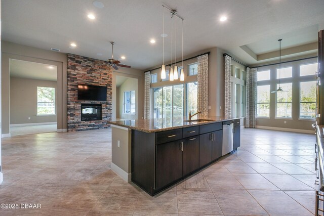 kitchen featuring open floor plan, hanging light fixtures, dark brown cabinets, and an island with sink