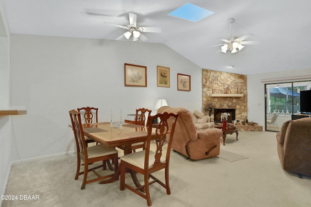 carpeted dining room with vaulted ceiling with skylight, ceiling fan, and a fireplace