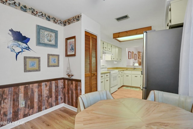 dining space with light wood-type flooring, sink, and wooden walls