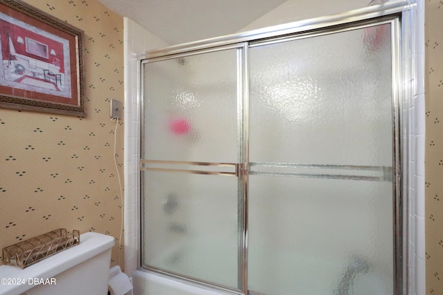 bathroom featuring toilet and bath / shower combo with glass door