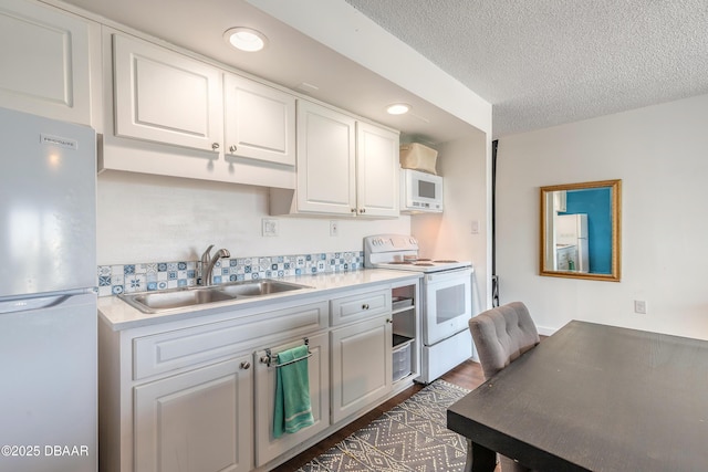 kitchen with white appliances, light countertops, white cabinets, a sink, and a textured ceiling