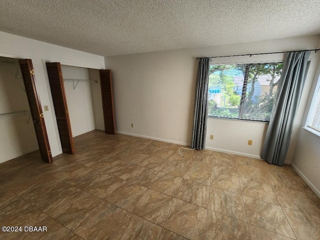 unfurnished bedroom with a textured ceiling and multiple closets