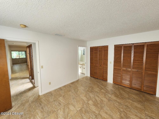 unfurnished bedroom with ensuite bathroom, a textured ceiling, and multiple closets