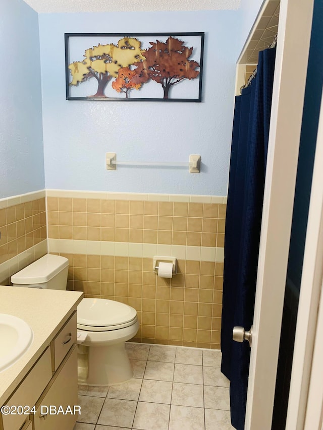 bathroom with toilet, vanity, tile walls, and tile patterned flooring