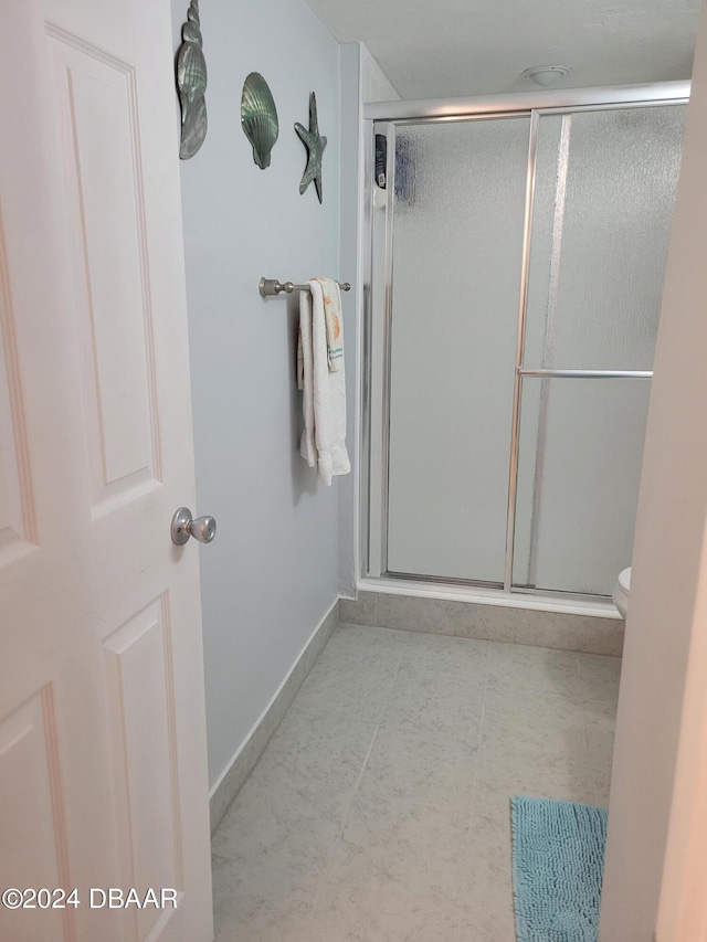 bathroom featuring tile patterned flooring, toilet, and a shower with shower door