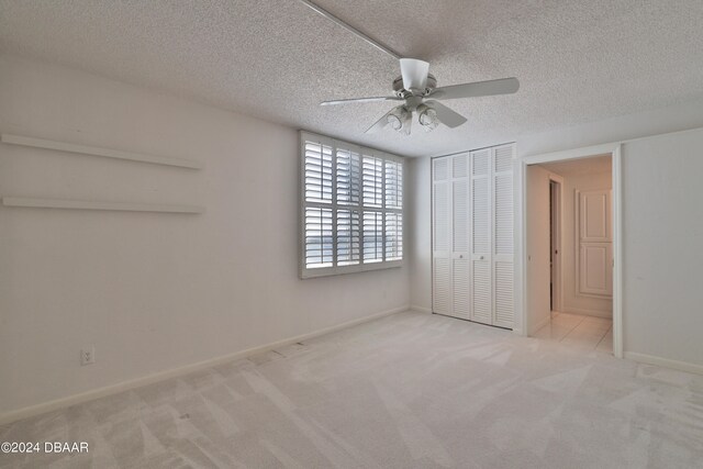 unfurnished bedroom featuring a closet, a textured ceiling, light colored carpet, and ceiling fan