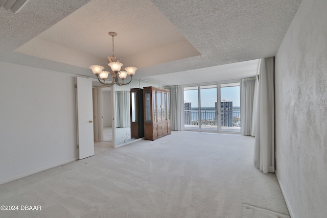 spare room with a water view, a notable chandelier, light carpet, and a tray ceiling