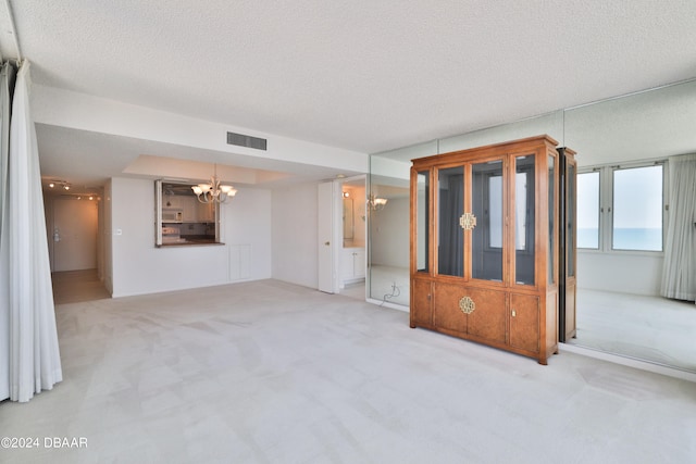 unfurnished living room featuring a textured ceiling, a notable chandelier, and light carpet