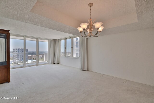 carpeted spare room featuring a tray ceiling, a chandelier, and a textured ceiling