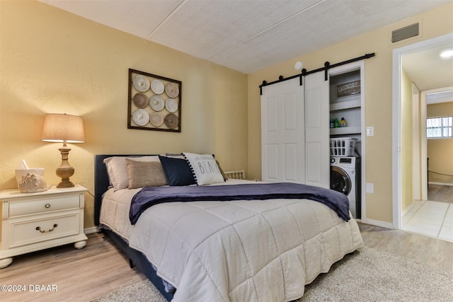 bedroom with washer / clothes dryer, light wood-type flooring, a barn door, and a textured ceiling