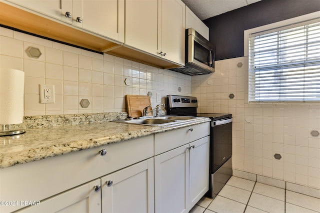 kitchen with stainless steel appliances, light tile patterned floors, sink, light stone countertops, and white cabinetry