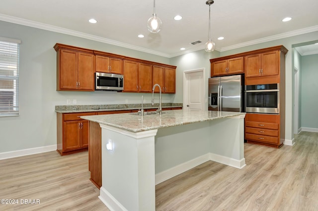 kitchen with light wood-type flooring, stainless steel appliances, hanging light fixtures, and an island with sink