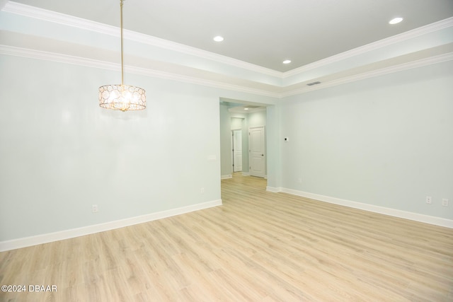 spare room featuring an inviting chandelier, ornamental molding, a tray ceiling, and light hardwood / wood-style flooring