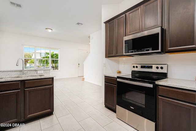 kitchen featuring stainless steel appliances, backsplash, light stone counters, and dark brown cabinetry