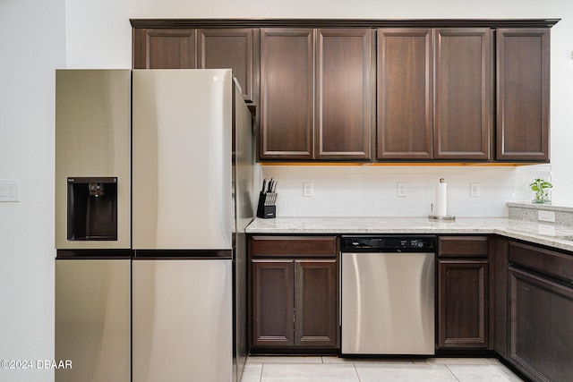 kitchen featuring stainless steel appliances, dark brown cabinetry, light stone countertops, light tile patterned floors, and decorative backsplash