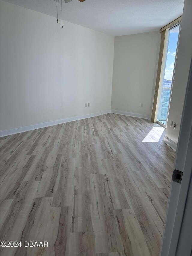 unfurnished room with floor to ceiling windows, ceiling fan, and light hardwood / wood-style floors