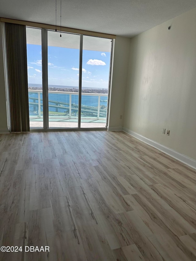 empty room featuring a healthy amount of sunlight, light hardwood / wood-style flooring, expansive windows, and a water view