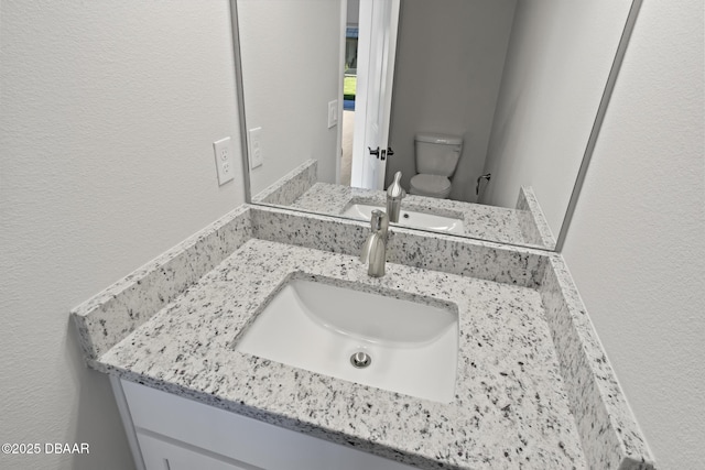 bathroom featuring a textured wall, toilet, and vanity