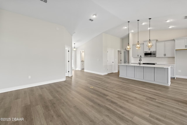 unfurnished living room with a sink, high vaulted ceiling, light wood-type flooring, and baseboards