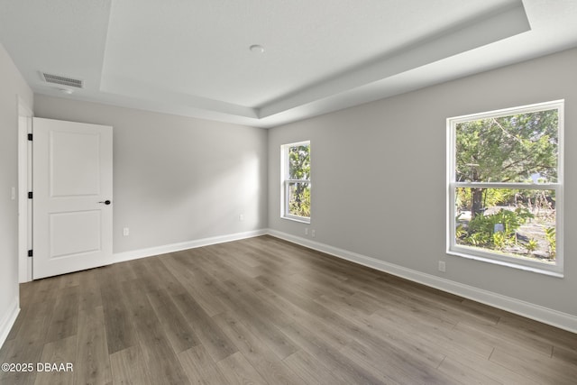 unfurnished room with a tray ceiling, dark wood finished floors, and baseboards