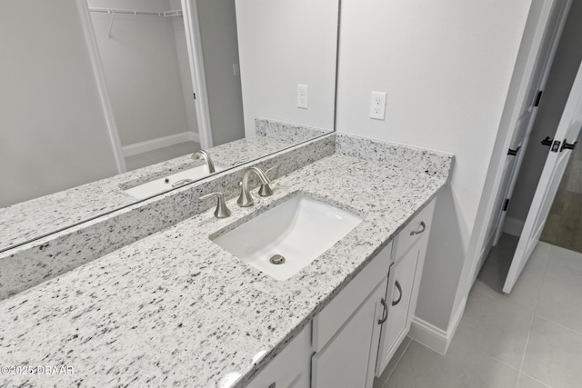 bathroom featuring tile patterned floors, vanity, baseboards, and a walk in closet