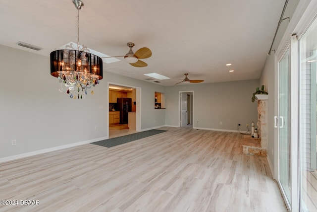 empty room with a skylight, light hardwood / wood-style flooring, and ceiling fan with notable chandelier