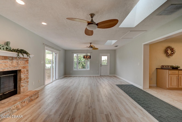 living room with light wood-type flooring, a skylight, a textured ceiling, ceiling fan, and a stone fireplace