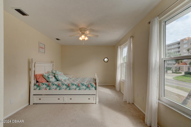 bedroom featuring ceiling fan, light colored carpet, and multiple windows