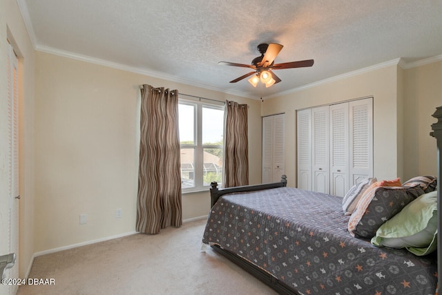 carpeted bedroom with multiple closets, a textured ceiling, ceiling fan, and ornamental molding