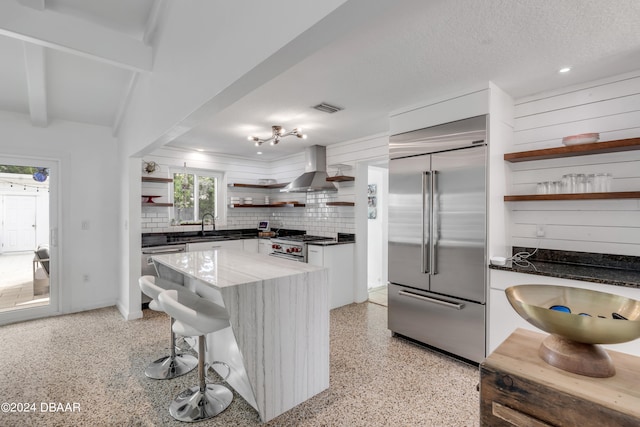 kitchen featuring tasteful backsplash, wall chimney range hood, a textured ceiling, white cabinets, and high end appliances