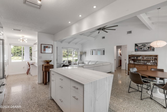 kitchen featuring lofted ceiling with beams, a kitchen island, white cabinetry, and a textured ceiling