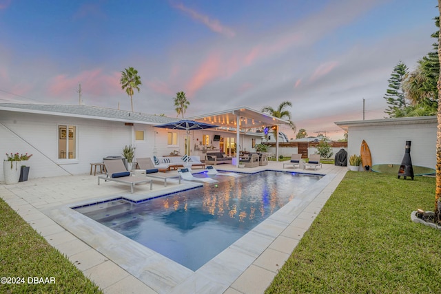 pool at dusk featuring a lawn, a patio, and an outdoor living space