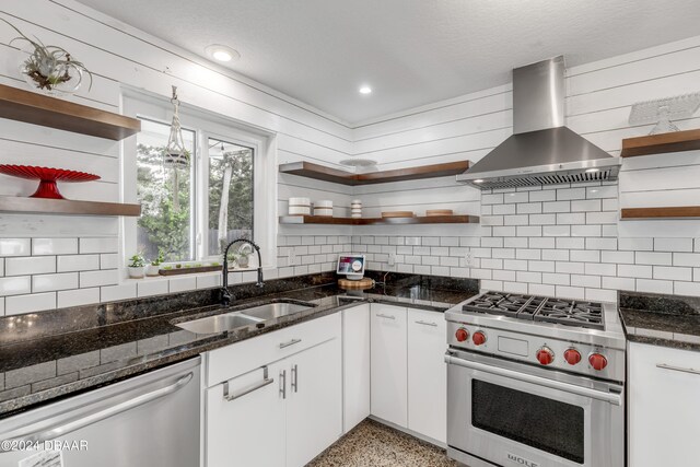 kitchen with sink, appliances with stainless steel finishes, tasteful backsplash, white cabinets, and wall chimney range hood