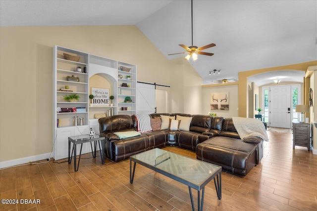 living room with a barn door, hardwood / wood-style flooring, ceiling fan, and vaulted ceiling