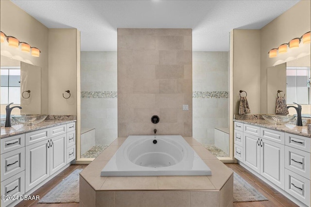 bathroom featuring vanity, tiled bath, hardwood / wood-style flooring, and a textured ceiling