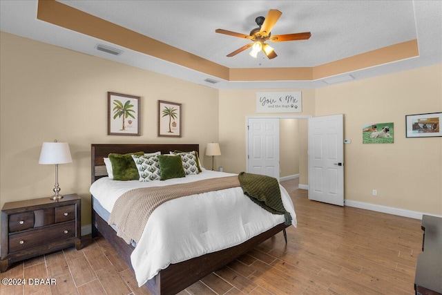 bedroom featuring a textured ceiling, hardwood / wood-style floors, ceiling fan, and a tray ceiling