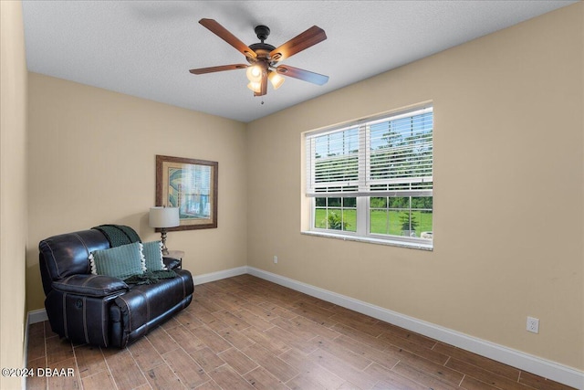 living area with ceiling fan, wood-type flooring, and a textured ceiling